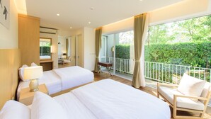 Habitación de hotel con dos camas, un escritorio, una silla y balcón con vistas a zonas verdes.