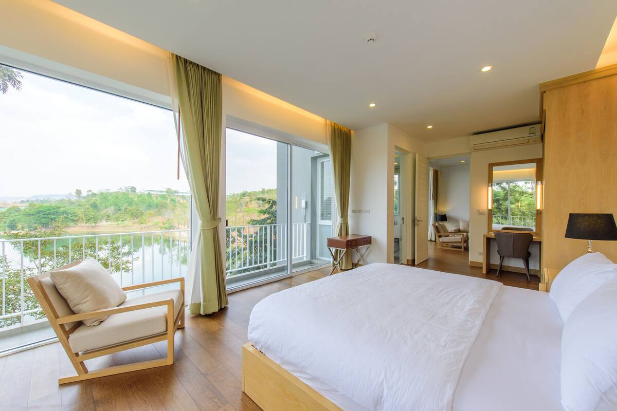Una habitación de hotel moderna con una cama grande, un balcón con vistas al verde, un escritorio y una silla.
