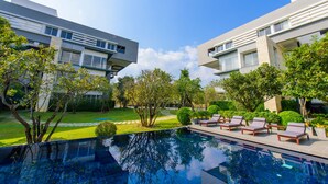 Un hotel moderno con piscina, sillas de descanso y jardines bien cuidados.