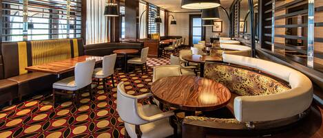 A modern restaurant with a patterned floor, round tables, and cushioned seating areas.