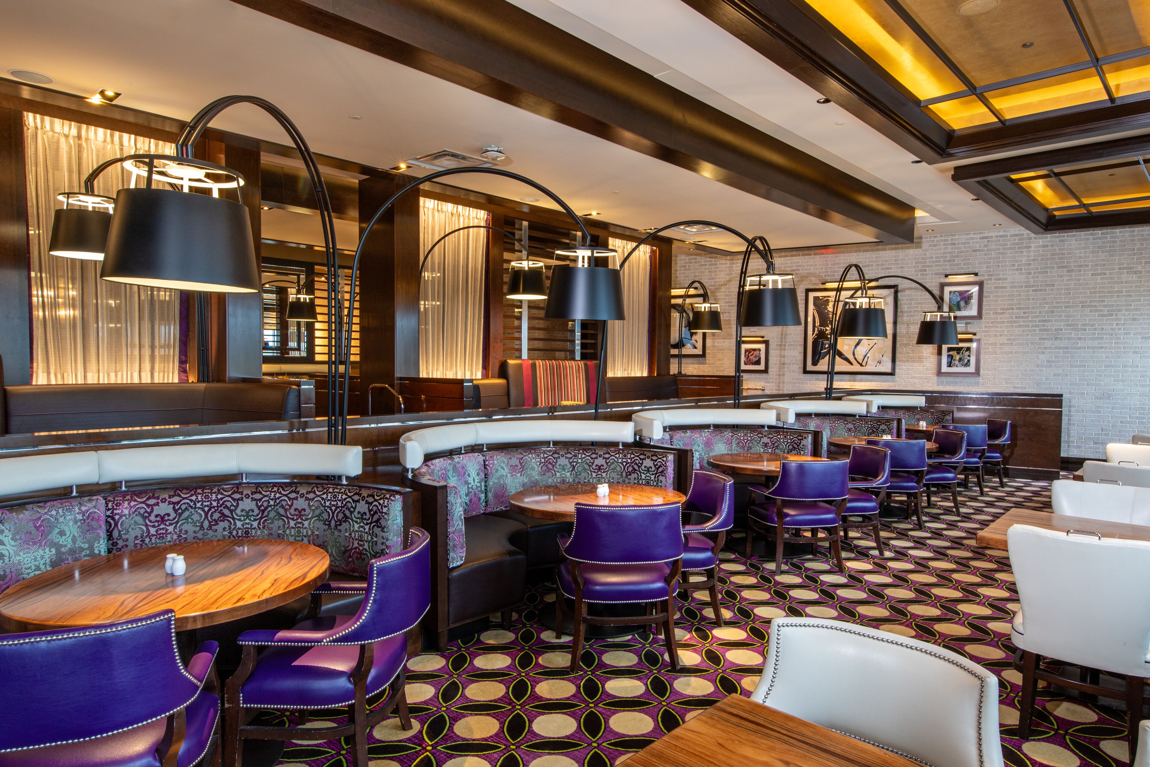 Un restaurante con mesas redondas y sillas moradas, con piso estampado e iluminación moderna.