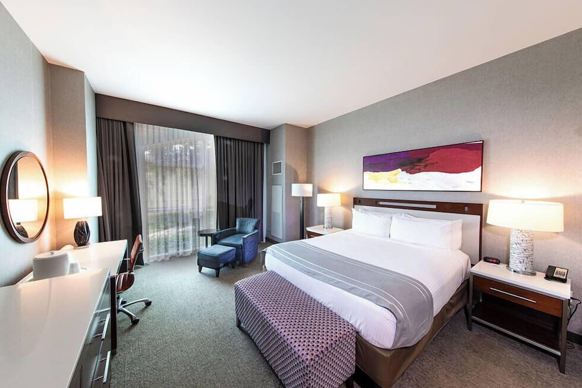 A hotel room with a large bed, a desk, a chair, a small table, and a window with curtains.