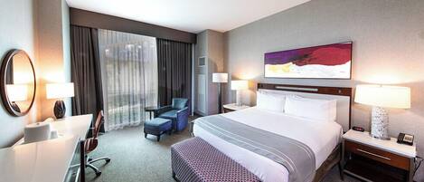 A hotel room with a large bed, a desk, a chair, a small table, and a window with curtains.
