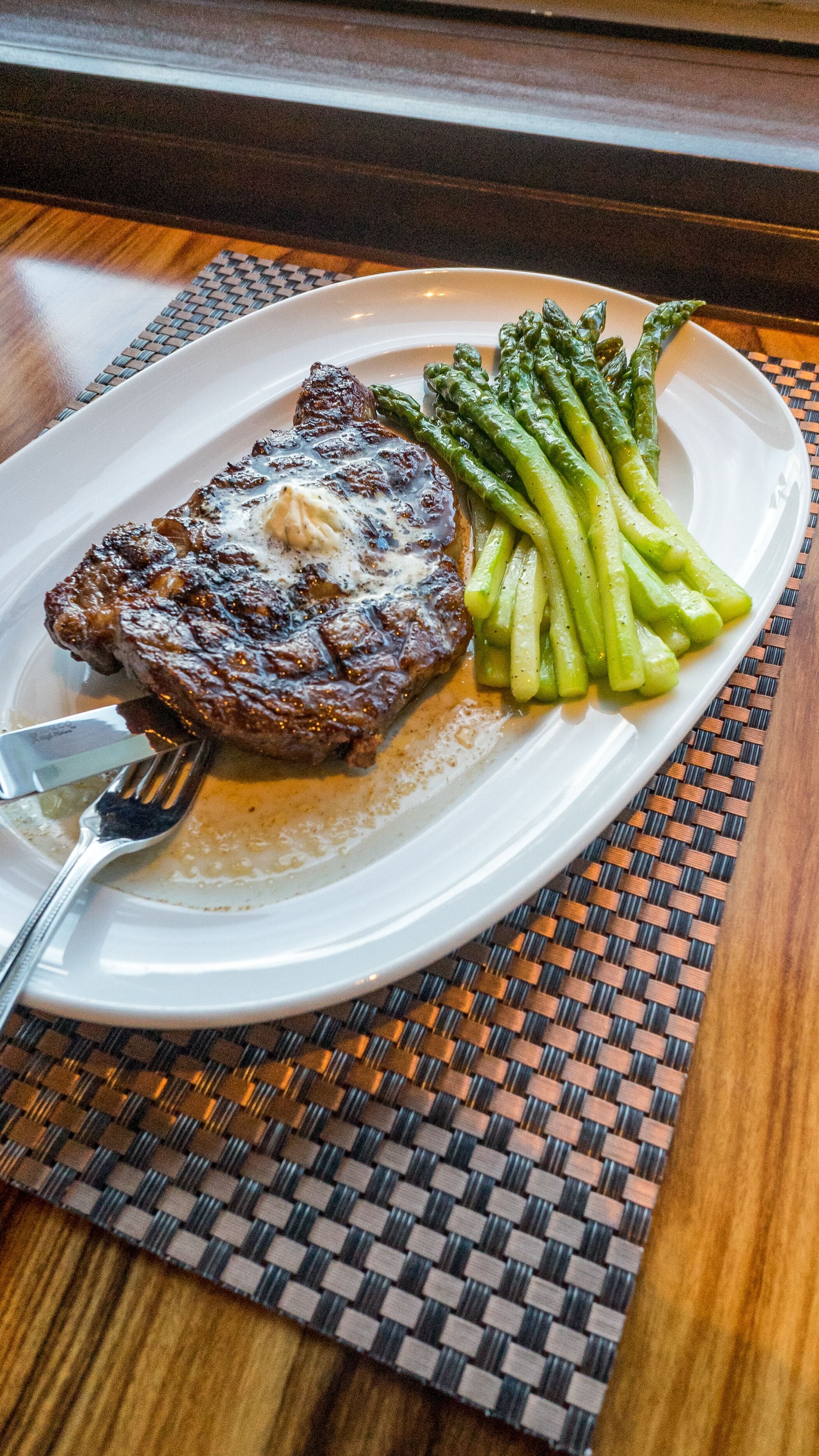 Un plato con bistec y espárragos sobre un posavasos tejido.