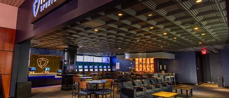 A sports bar with multiple screens, seating areas, and a bar counter.