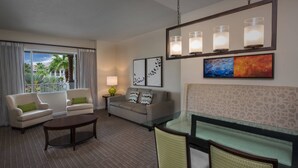 Ein Hotelzimmer mit Sofa, Sesseln, einem Glastisch und Blick auf Palmen.