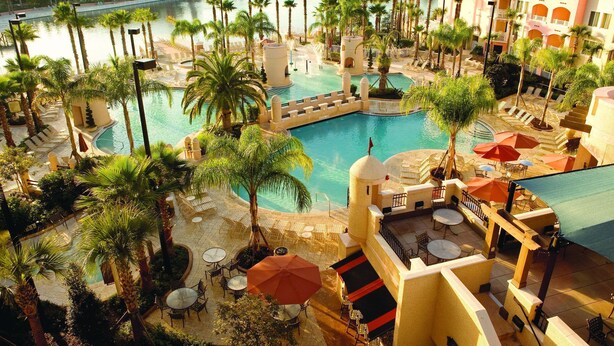 Ein Resort mit mehreren Pools, umgeben von Palmen und Liegebereichen mit Sonnenschirmen.