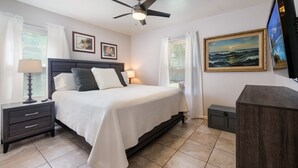 A bedroom with a bed, nightstands, a ceiling fan, a TV, and artwork on the walls.