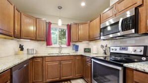 A kitchen with wooden cabinets, stainless steel appliances, a granite countertop, and a window with red curtains.