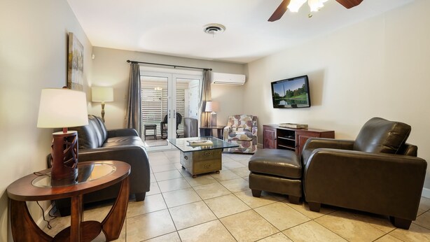 A living room with a glass coffee table, leather sofas, a wooden side table, and a ceiling fan.