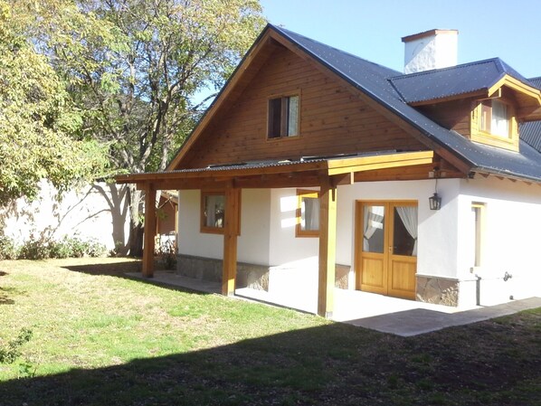 A two-story wooden house with a covered porch, a stone foundation, and a chimney.