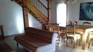 Una sala de estar acogedora con una escalera de madera, un sofá estampado, una mesa de comedor con sillas y un cuadro grande en la pared.