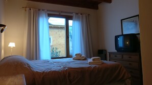 Un dormitorio con cama, televisor, lámpara y ventana con cortinas.