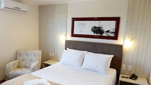 Una habitación de hotel con una cama, una silla, una mesita de noche con teléfono y un cuadro en la pared.