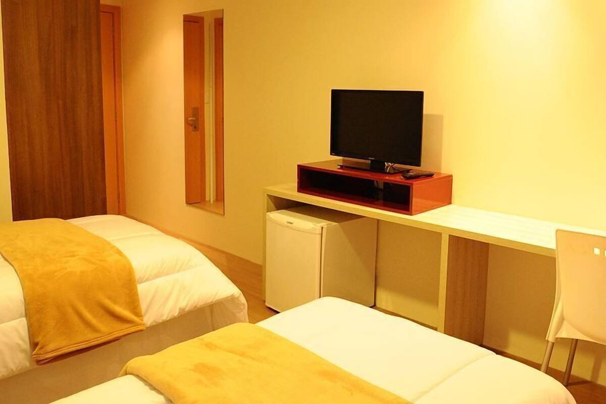 A hotel room with two beds, a TV on a stand, a small fridge, and a desk.
