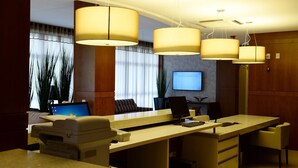 Zona de recepción de un hotel con un mostrador largo, varias sillas, una pantalla de televisión y lámparas colgantes.