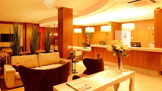 Un hall de hotel con un sofá, sillas, una mesa, mostrador de recepción y un televisor.