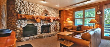 Una sala de estar acogedora con chimenea de piedra, sofá de cuero y televisor.