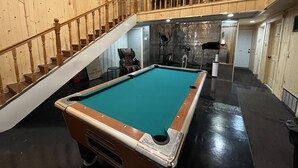 Una mesa de billar en una sala con paredes de madera y una escalera.