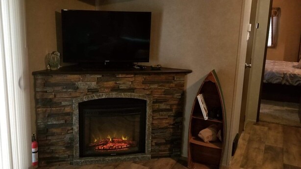 Una chimenea de piedra con un televisor encima, una estantería y una puerta que da a otra habitación.