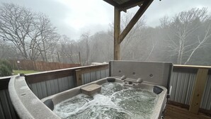 Jacuzzi con cubierta de madera y techo metálico, rodeado por una valla de madera y árboles.