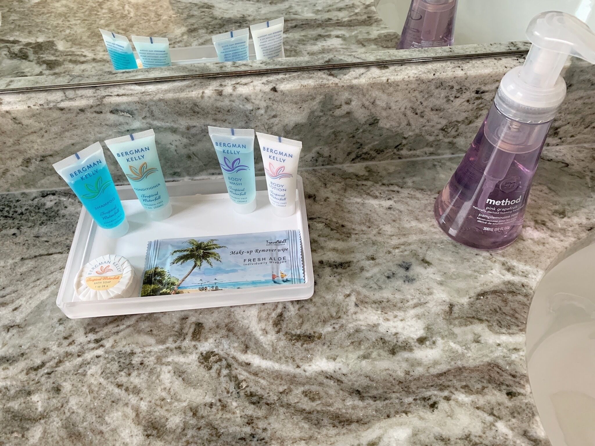 Una encimera de baño con varios productos para el cuidado de la piel Bergman Kelly, un jabón corporal Method de pomelo rosa y una toallita desmaquillante de viaje.