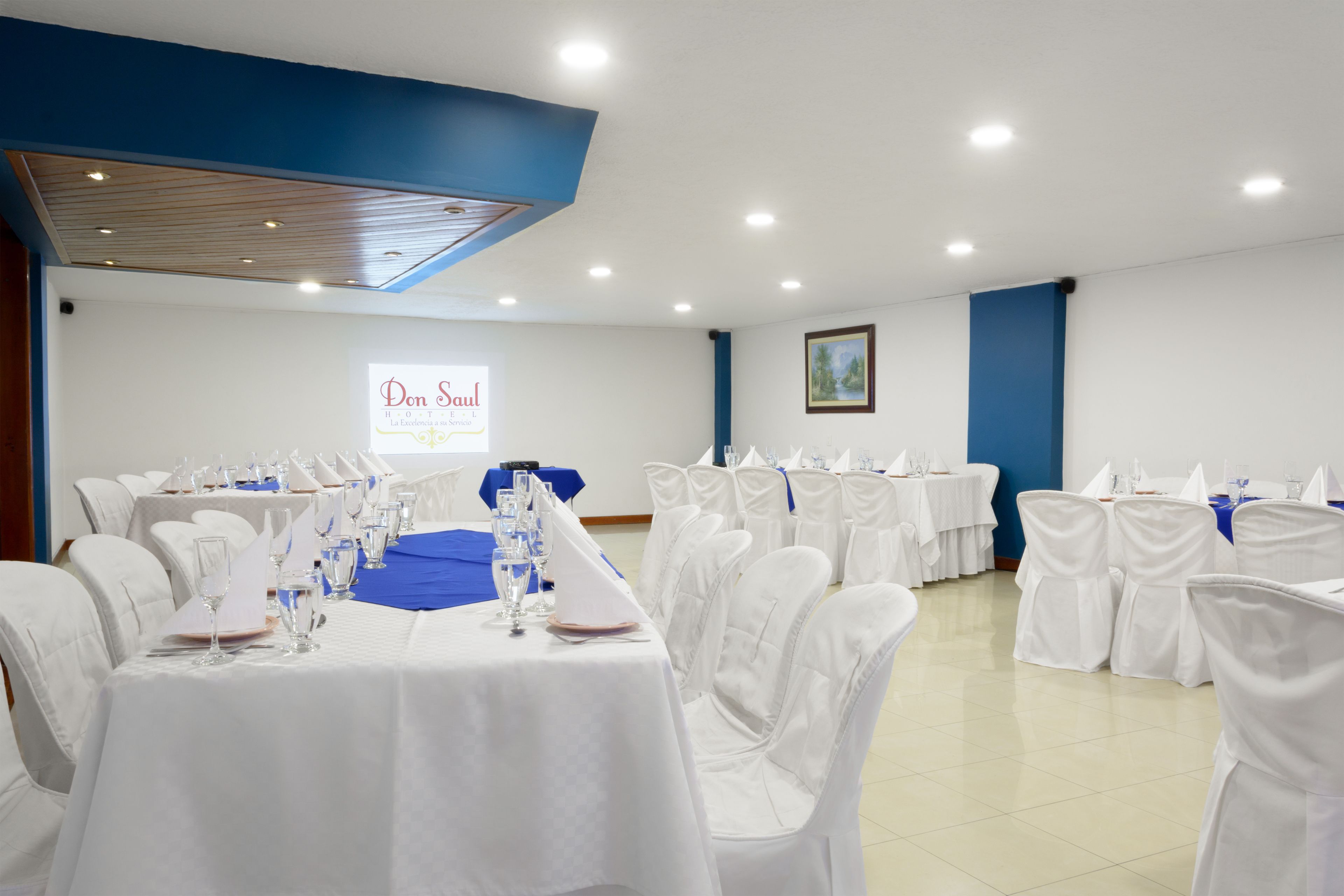 A banquet hall with white tables and chairs, a blue accent wall, and a sign reading "Don Saul".