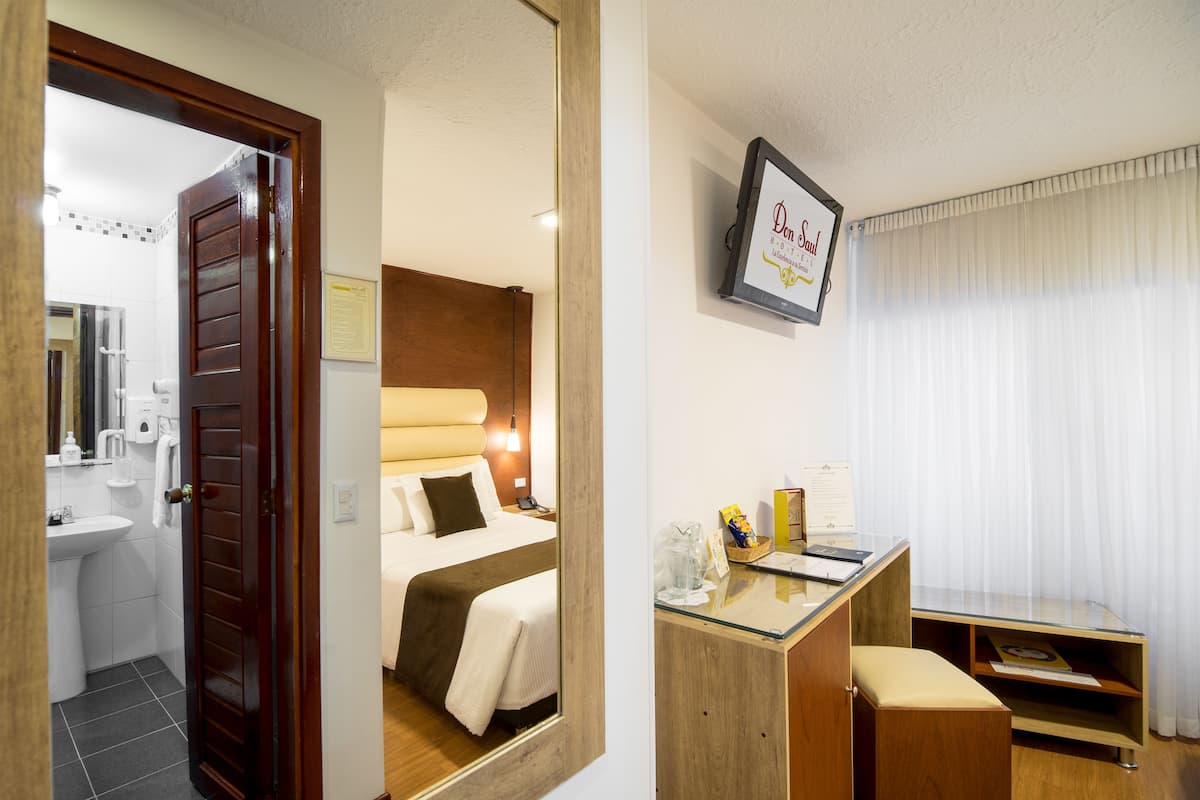 Una habitación de hotel con una cama, mesita de noche y un escritorio con silla.