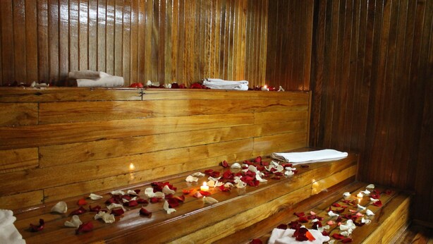 Un espacio de spa de madera con bancos, toallas y pétalos de rosa esparcidos.