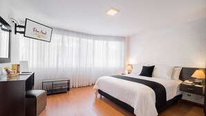 Una habitación de hotel moderna con una cama grande, mesitas de noche, un escritorio y un televisor montado en la pared.