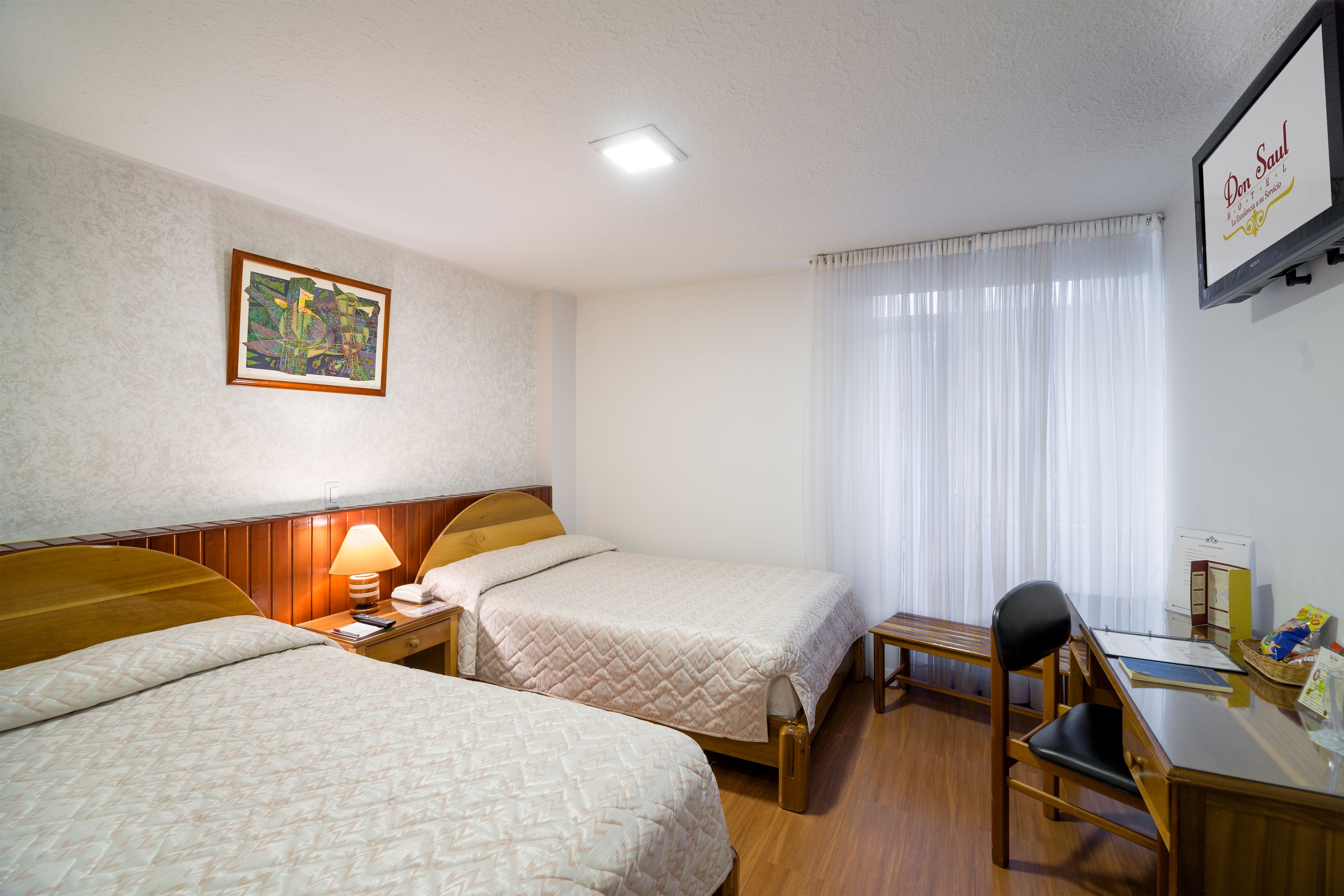 Une chambre d’hôtel avec deux lits, un bureau, une chaise, une lampe et un tableau au mur.