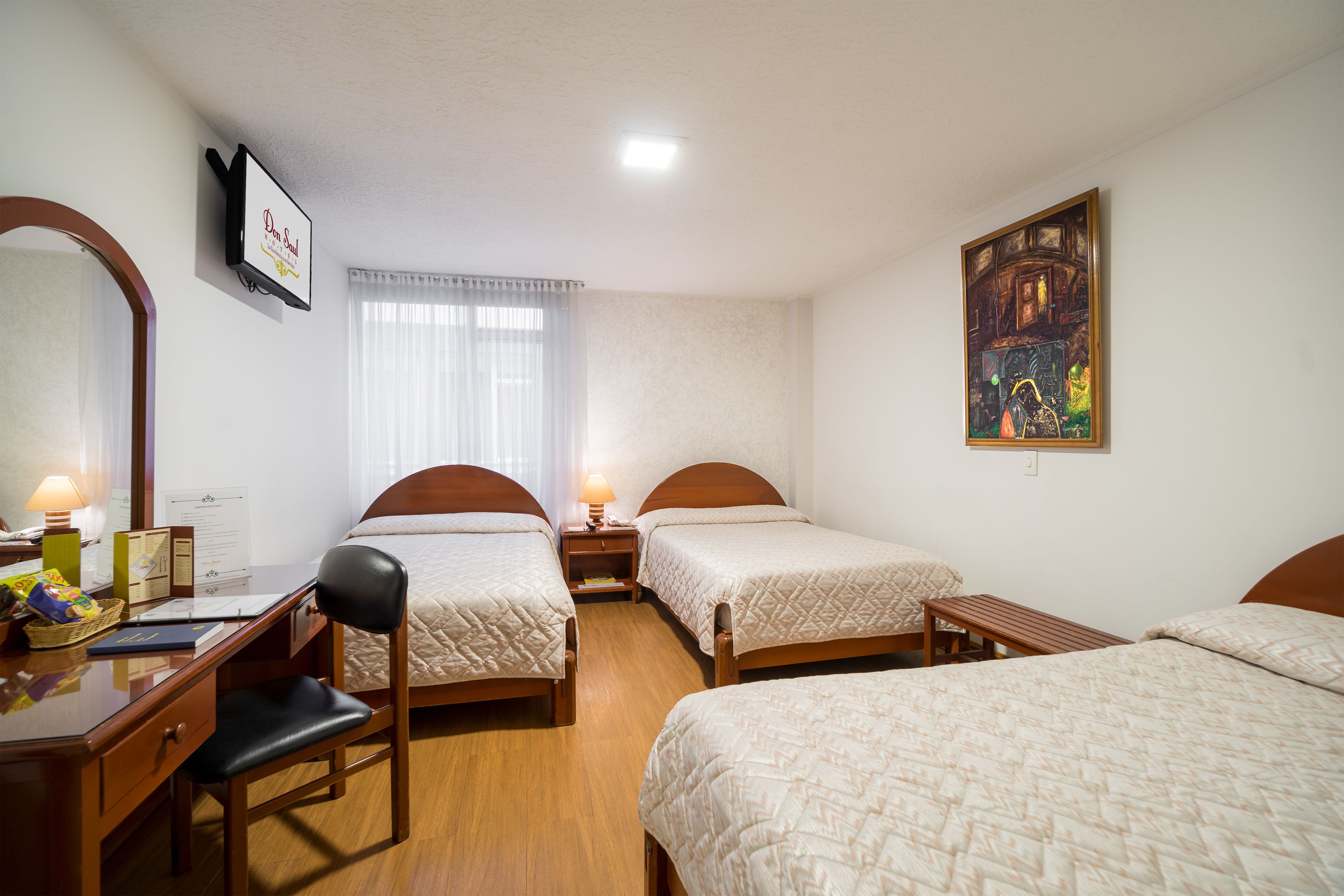 Habitación de hotel con dos camas individuales, un escritorio con silla, un televisor y un cuadro en la pared.