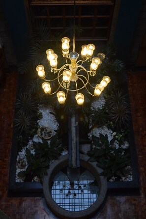 Un candelabro con múltiples bombillas, rodeado de plantas decorativas y un elemento acuático circular.