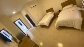 Une chambre d’hôtel avec deux lits, un bureau, une chaise, une télévision et une porte donnant sur l’extérieur.