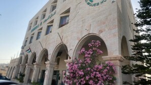 Un bâtiment arborant le logo de l’hôtel Al-Mujeb, caractérisé par un style architectural moderne avec des fenêtres en arc de cercle et une façade en pierre.