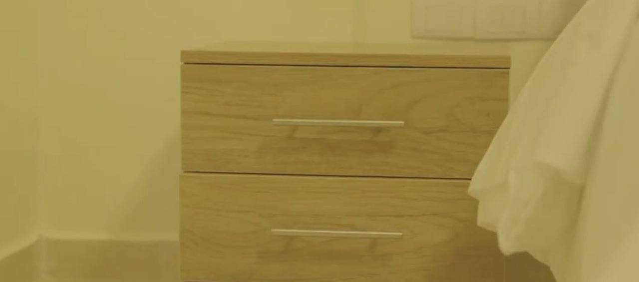 Una mesita de noche de madera con dos cajones y una toalla blanca colgada en la pared.