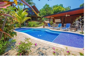 Relax by the serene pool surrounded by lush tropical vegetation and shaded by a thatched roof.