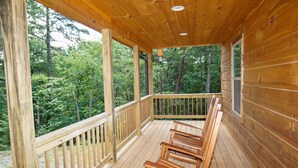 A wooden deck with a railing, benches, and a view of a forest. - Cabin in the Woods-Gas Fireplace - Charcoal Grill - Pet Friendly (Whittier)