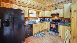 Cocina de cabaña de madera con un refrigerador negro, armarios de madera, una estufa y un microondas.