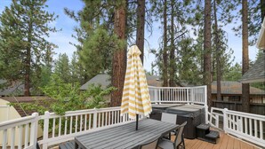 A deck with a table and chairs, a striped umbrella, and a white railing. - Southern Comfort - AC, Hot Tub,Centrally Located, Fenced Yard, BBQ (Big Bear Lake)