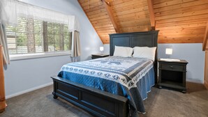 A bedroom with a wooden ceiling, a bed with a patterned bedspread, two bedside tables, and a window with blinds. - Southern Comfort - AC, Hot Tub,Centrally Located, Fenced Yard, BBQ (Big Bear Lake)