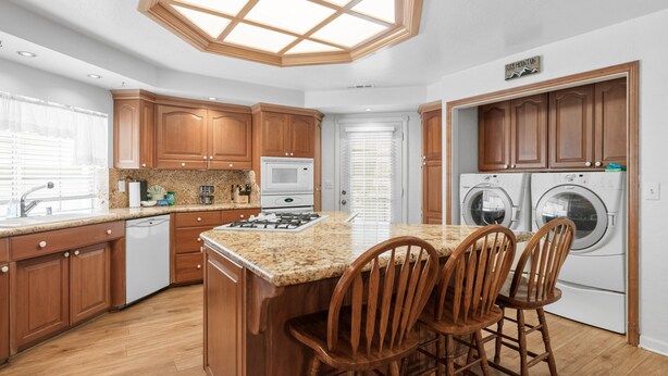 A modern kitchen with wooden cabinets, a granite countertop, a built-in oven, a microwave, and a dishwasher. There are two wooden chairs at a small island. - Southern Comfort - AC, Hot Tub,Centrally Located, Fenced Yard, BBQ (Big Bear Lake)
