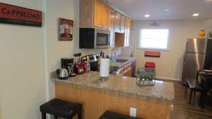 A kitchen with wooden cabinets, a granite countertop, a coffee maker, a blender, and two stools.