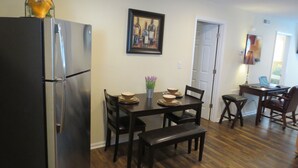 A compact kitchen with a refrigerator, dining table, chairs, and a laptop on a desk.