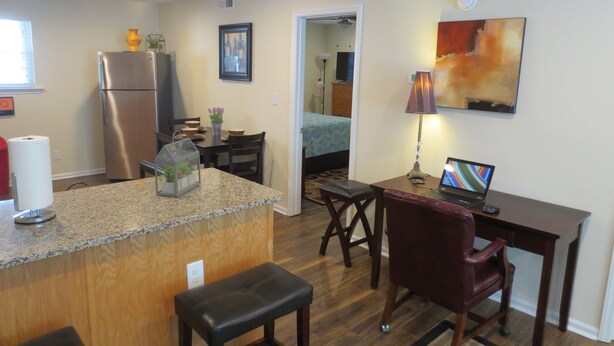 A compact kitchen with a refrigerator, dining table, and a laptop on a desk.