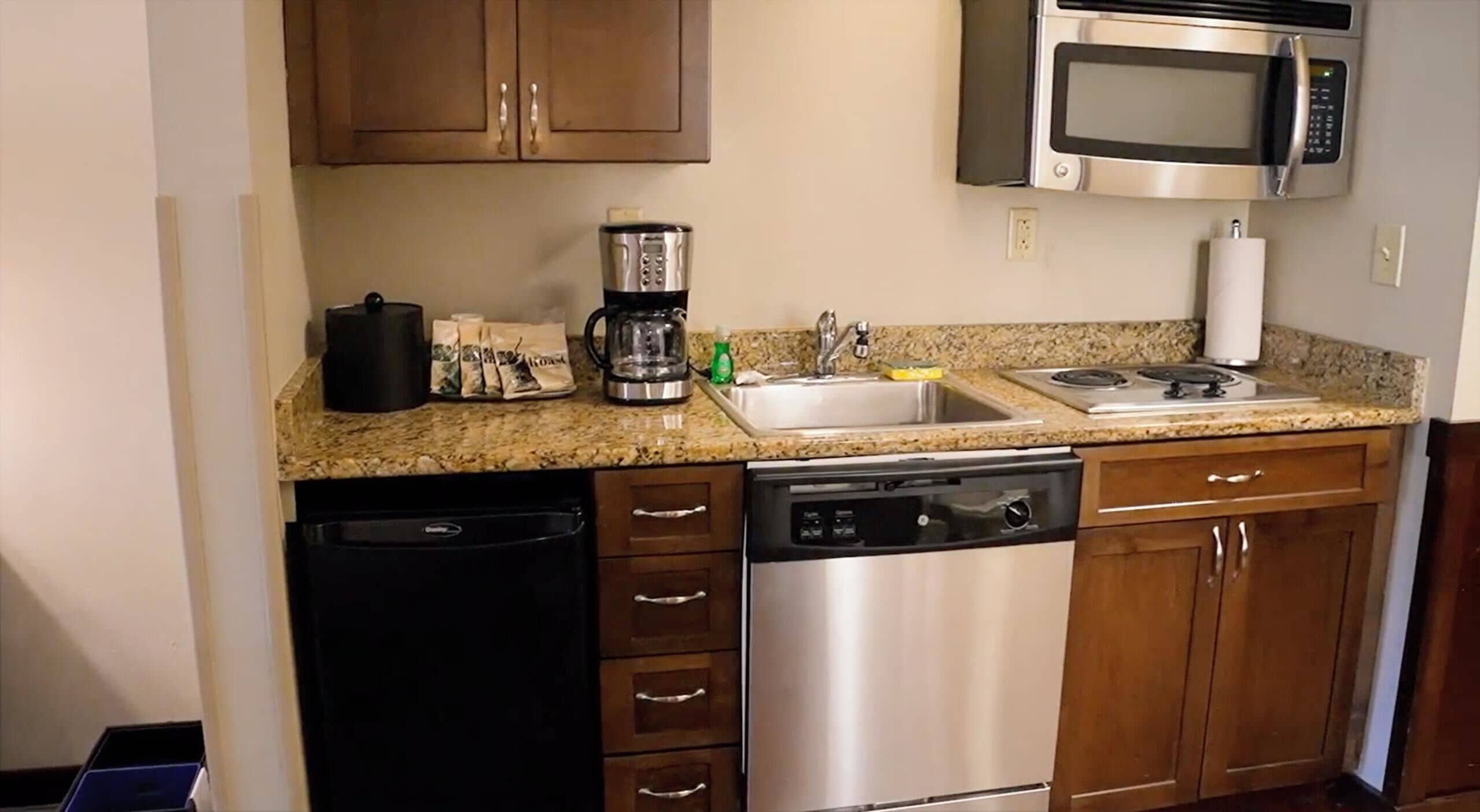 A compact kitchen with a dishwasher, stove, microwave, and a coffee maker.