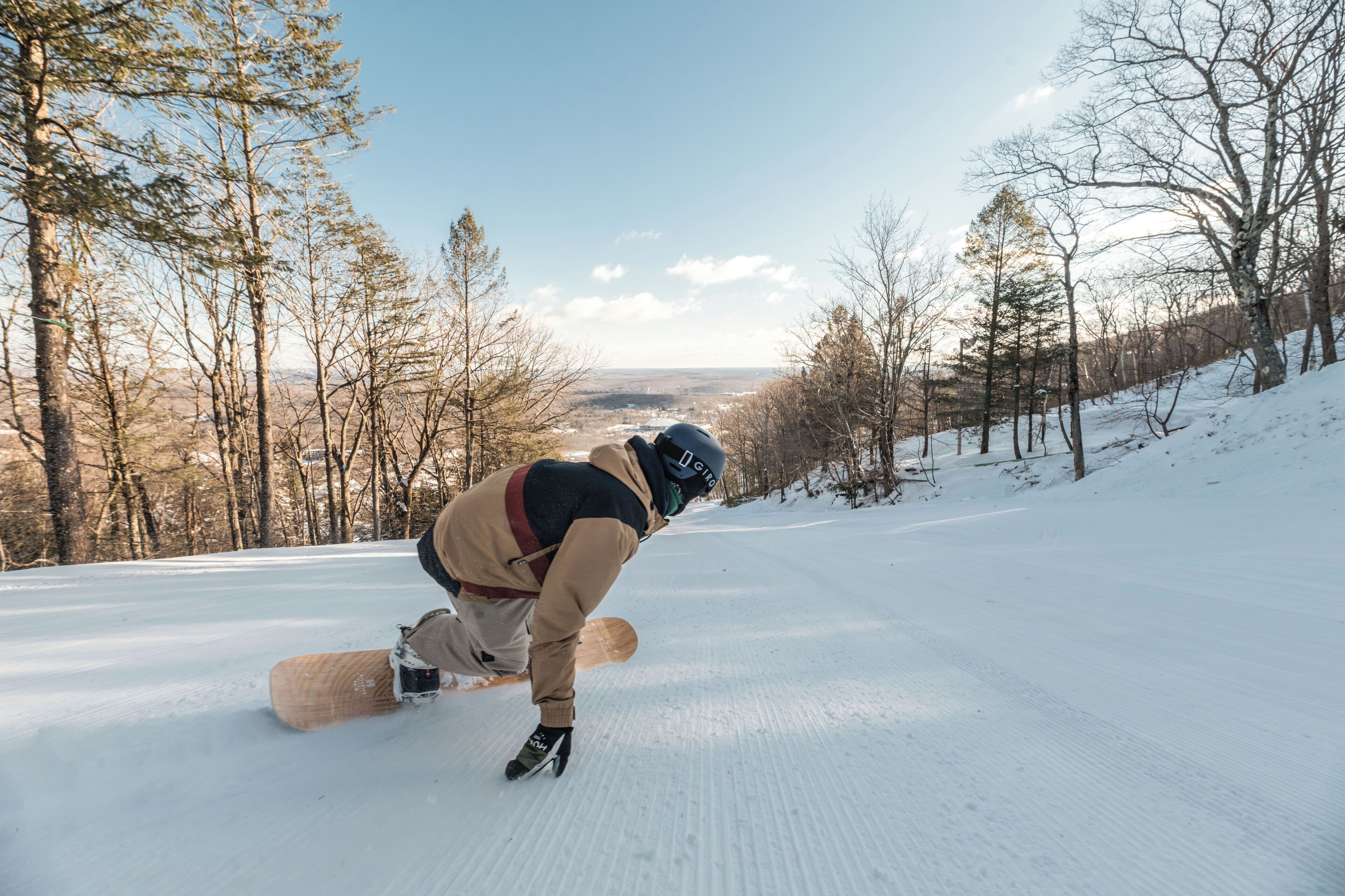 A snowboarder on a snowy slope with trees and a clear sky.
