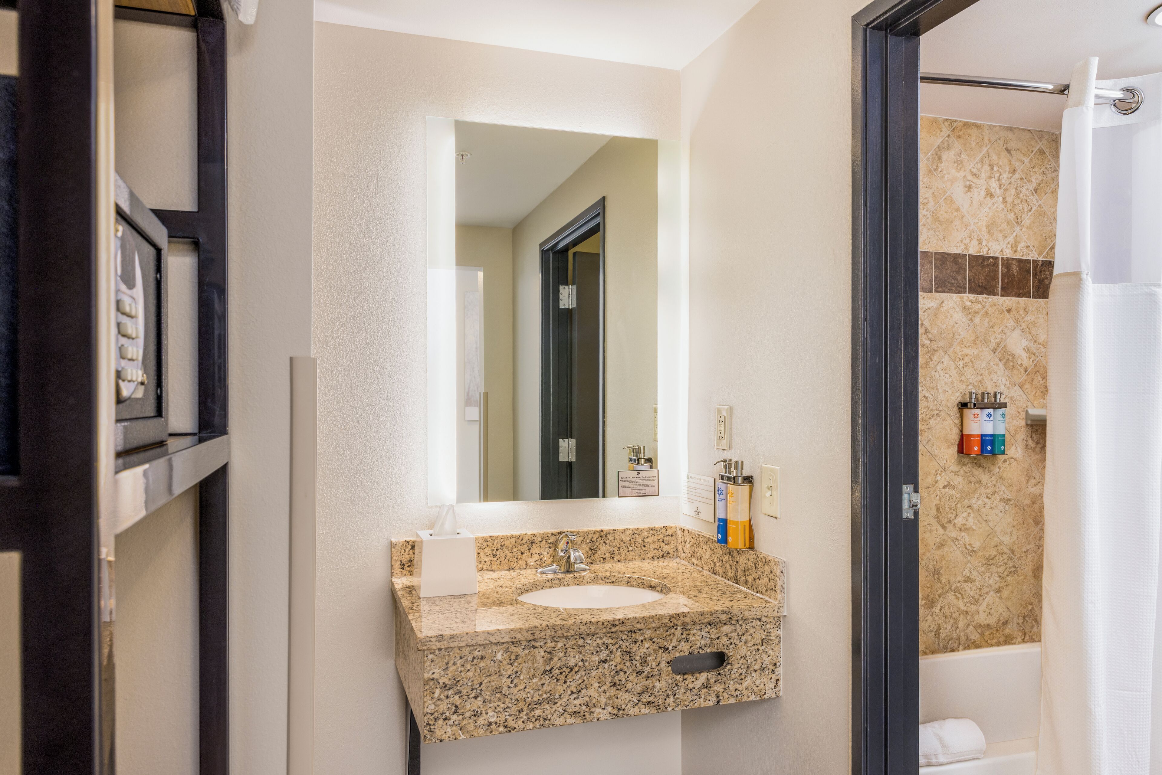 A bathroom with a granite sink, a mirror, a towel rack, and a shower area.