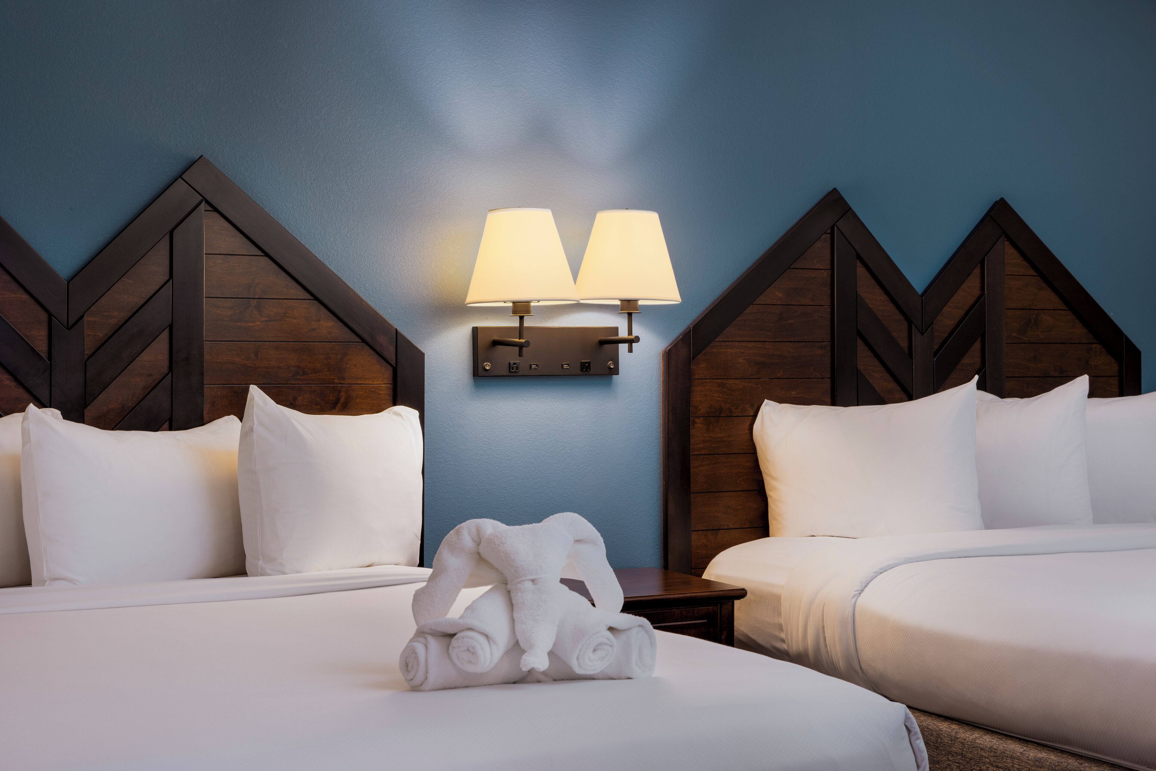Una habitación de hotel con dos camas, una lámpara de pared y una toalla doblada cuidadosamente sobre la cama.