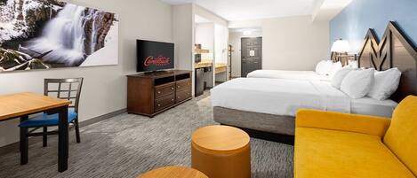 Hotelkamer met een bed, een televisie, een bureau met stoel, een bank en een ronde houten tafel.
